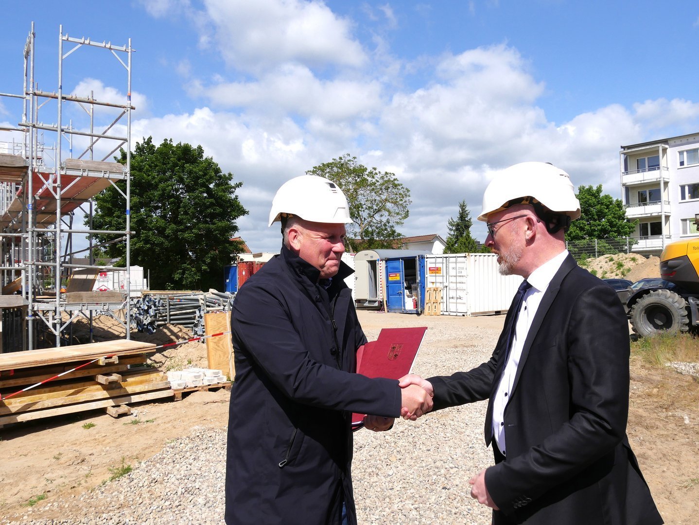 Übergabe von unterlagen, auf der Baustelle, die Personen schütteln die Hände, beide Lächeln. 